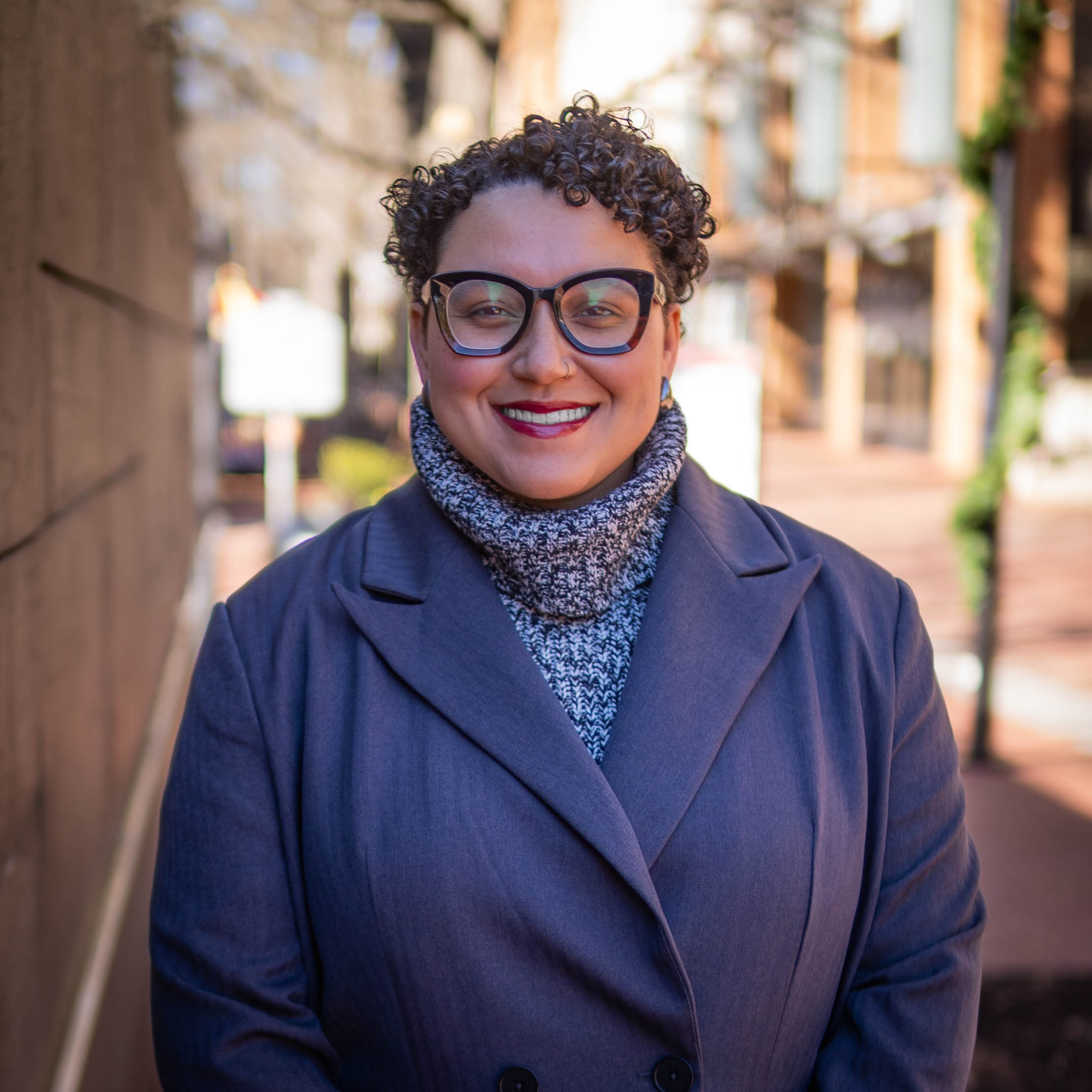 Smiling woman in gray coat with thick rim glasses